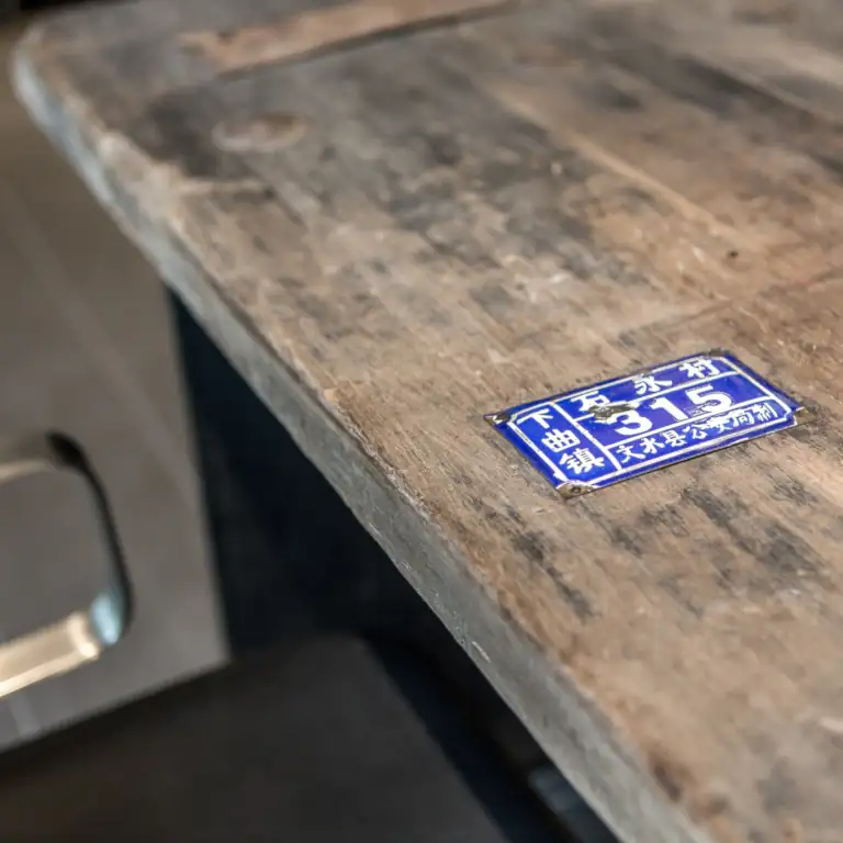 Nahaufnahme eines zur Tischplatte umfunktionierten hölzernen Scheunentores mit einer blauen Plakette, beschriftet mit chinesischen Schriftzeichen.